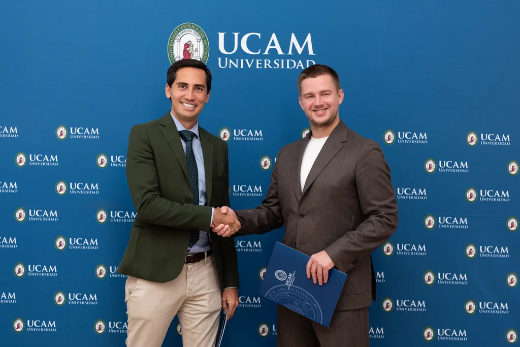 Representatives shaking hands in front of the UCAM university backdrop